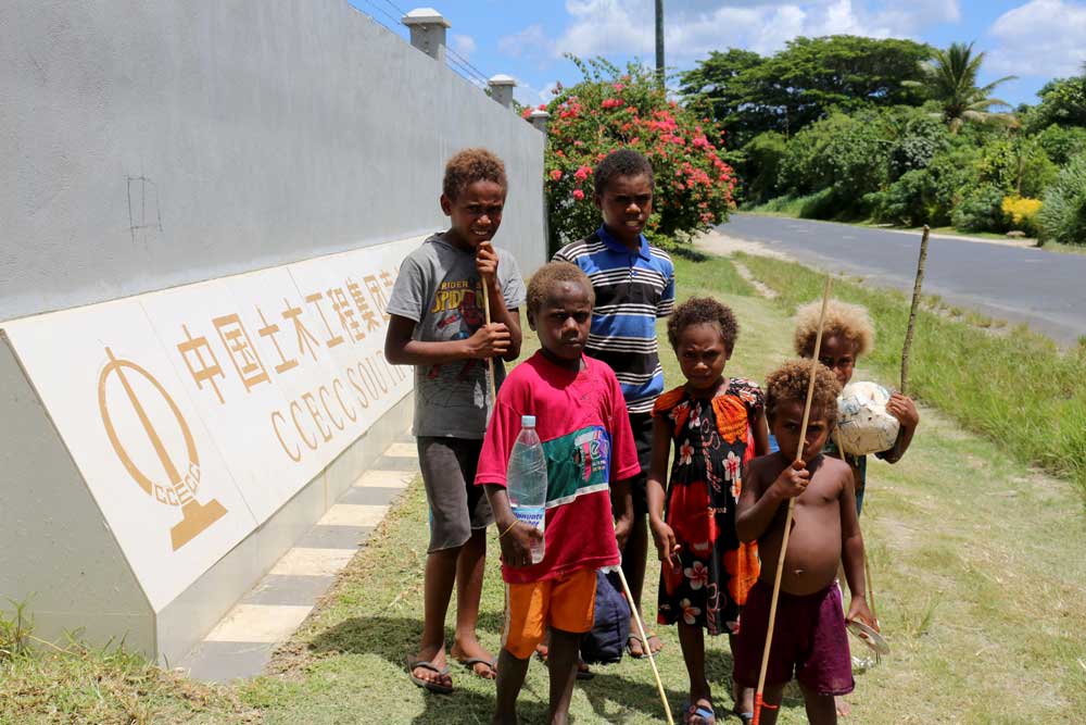 A group of children with fishing spears walk to the beach and past a large commercial Chinese bank. Photo: RFA