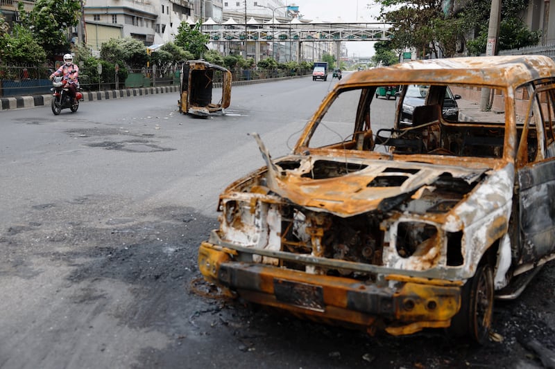 A man rides his motorbike on a mostly empty street past vehicles that were set on fire during clashes among university students, police and government supporters, after violence erupted during what were initially protests against government job quotas,Dhaka, July 22, 2024. (Mohammad Ponir Hossain/Reuters)
