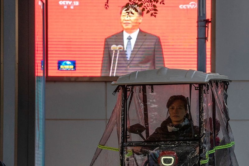 一名骑着三轮车的妇女在北京经过显示中国国家主席习近平的屏幕。(美联社)